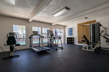A gym with weights and cardio equipment in a building with windows
